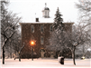 An outside winter view of town hall with snow and lighted lamp