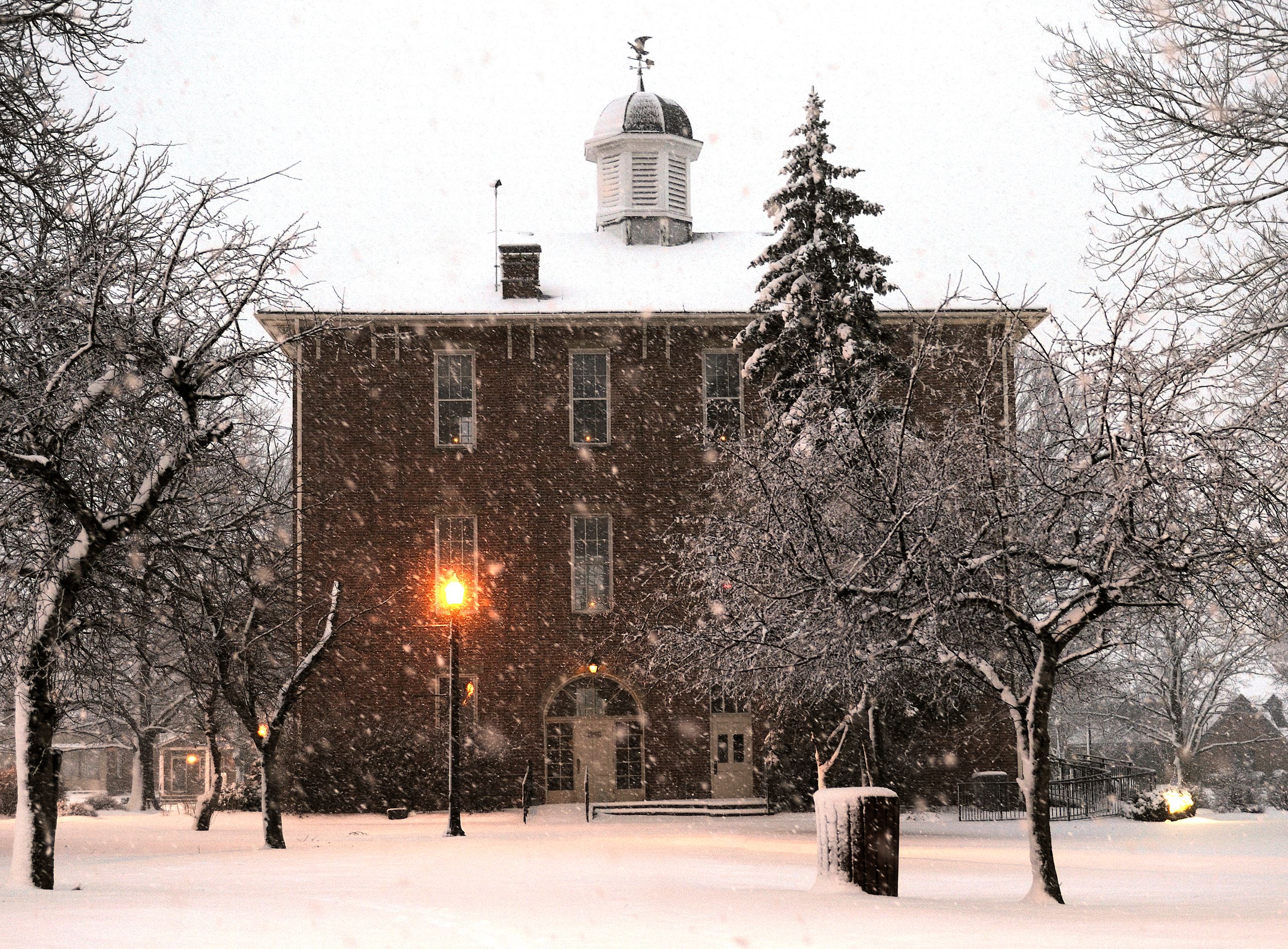An outside winter view of town hall with snow and lighted lamp